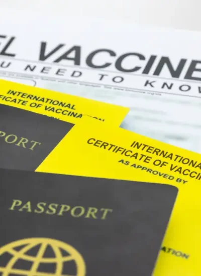 Travel passports, travel vaccines checklist, and country flags arranged on a desk for international trip preparation.